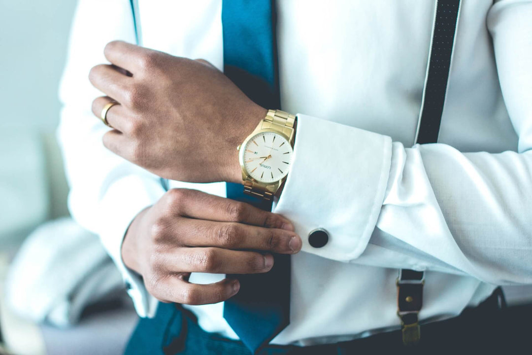 A white men touches his cufflinks. He's wearing a golden watch.